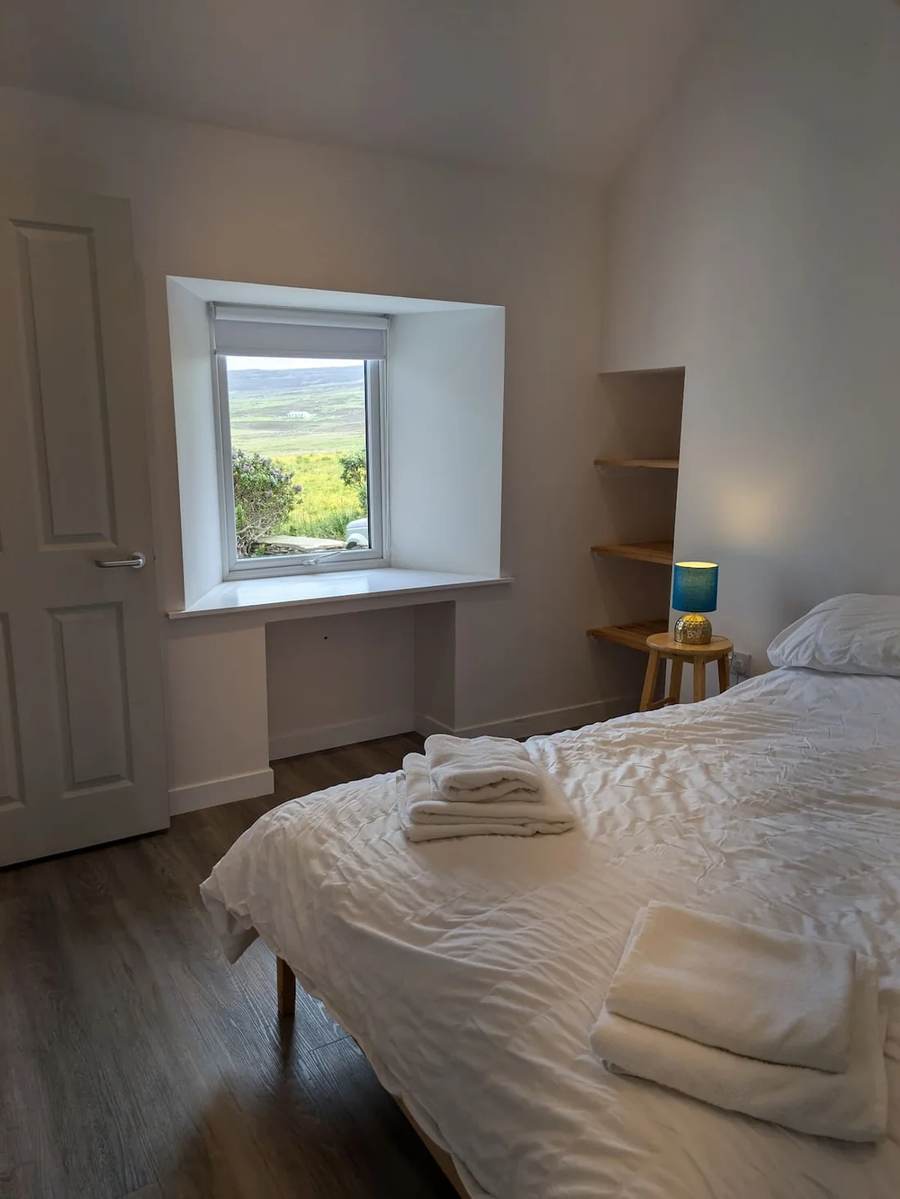 King-size bed with folded towels beside a blue lamp and a window overlooking fields