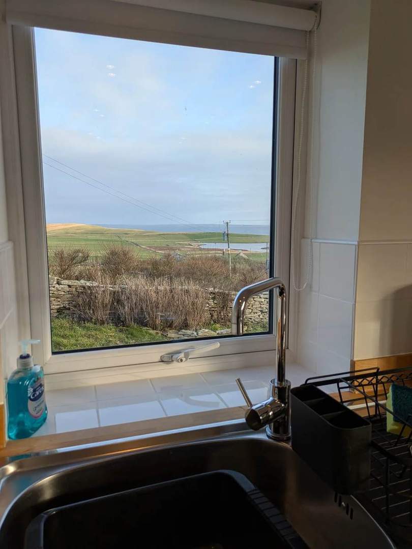 Kitchen sink beneath a window overlooking fields and the sea