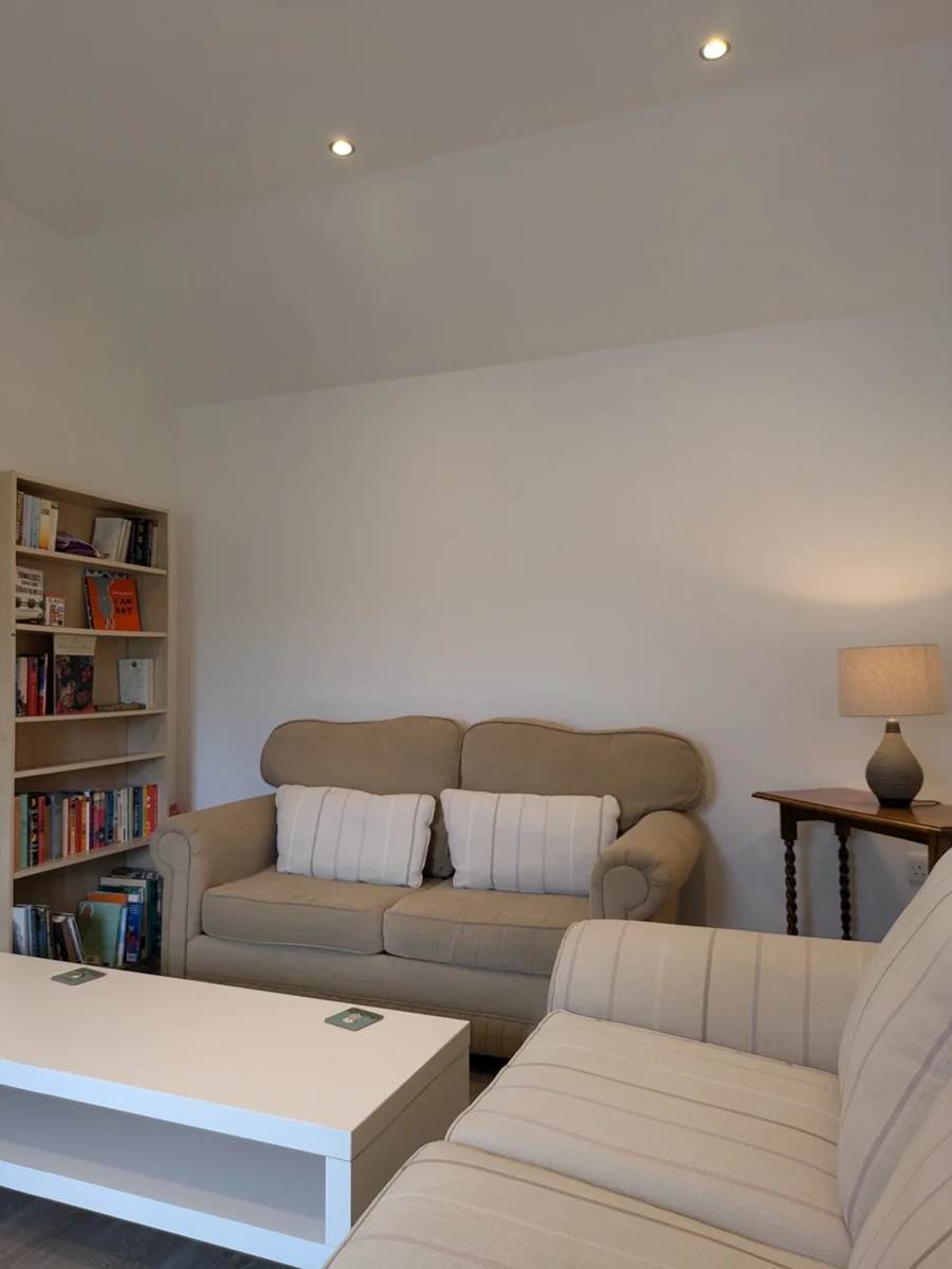 Sofas, a coffee table and a bookcase beneath the high ceiling in The Cottage living room
