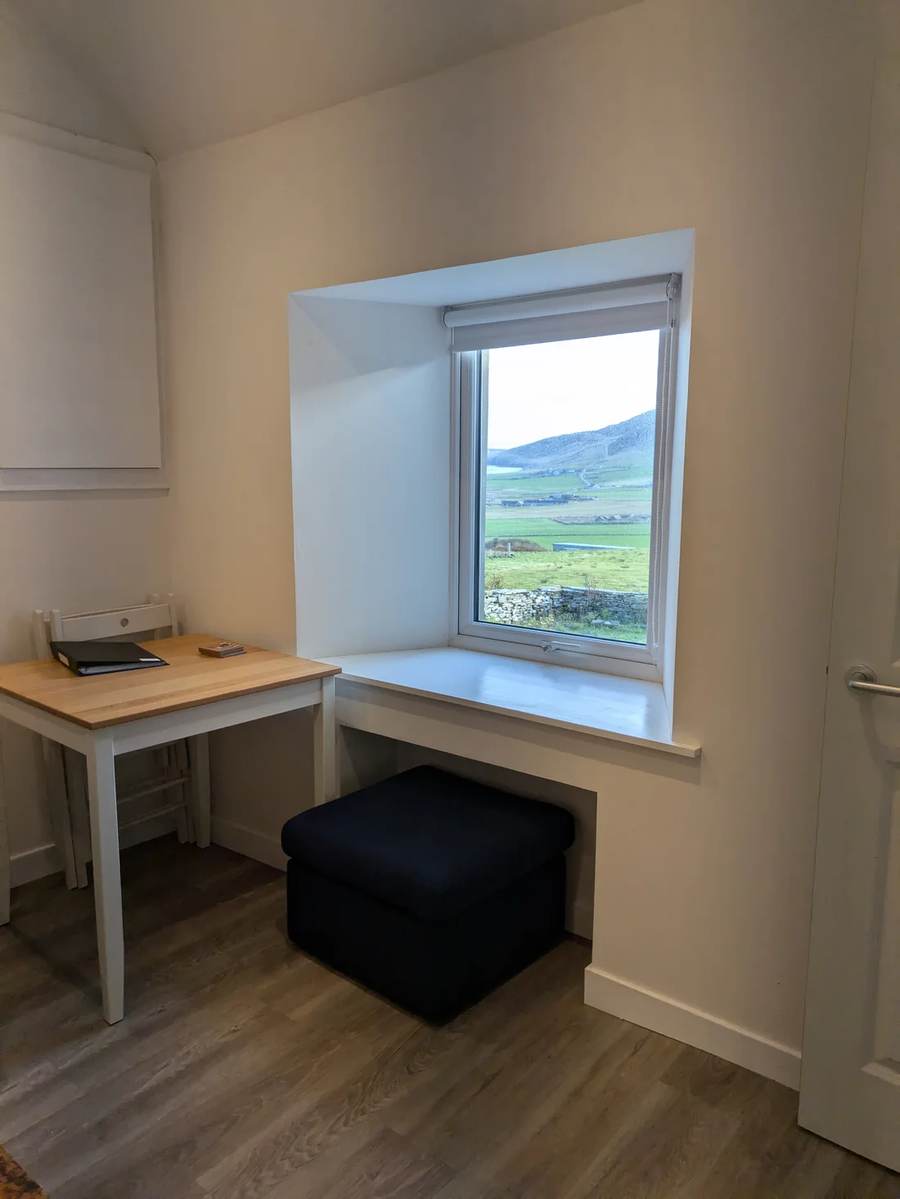 A table and deep window in The Cottage overlooking green fields and hills