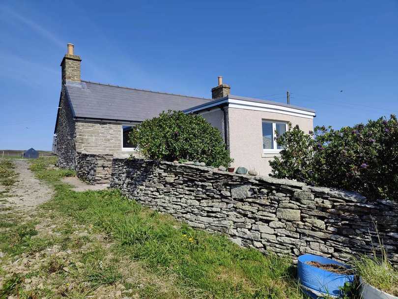 Stone exterior of The Cottage behind its garden wall