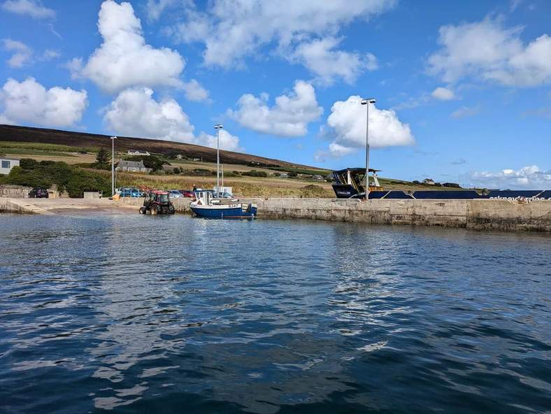 The Eynhallow ferry and a small boat alongside a stone pier, with hillside houses behind