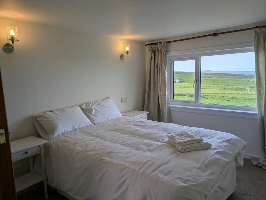 King-size bed with white bedding beside a window overlooking fields