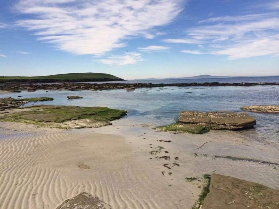 A sandy stretch of the Rousay coast with rock shelves and blue sea
