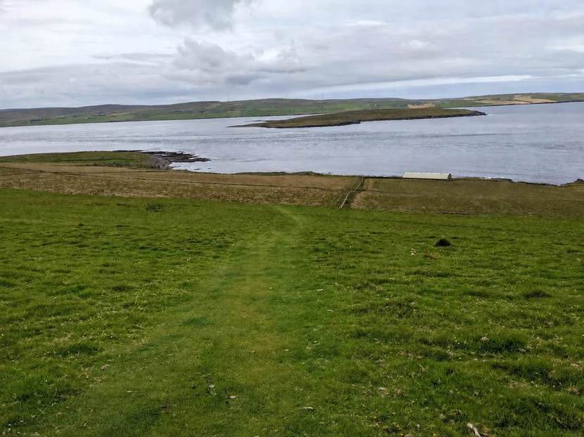 Grass path leading downhill towards Midhowe Cairn and the shore, with Eynhallow island across the water