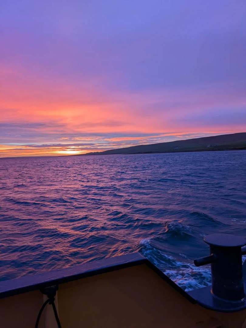 Early morning light above the sea and a dark coastline, seen from the ferry