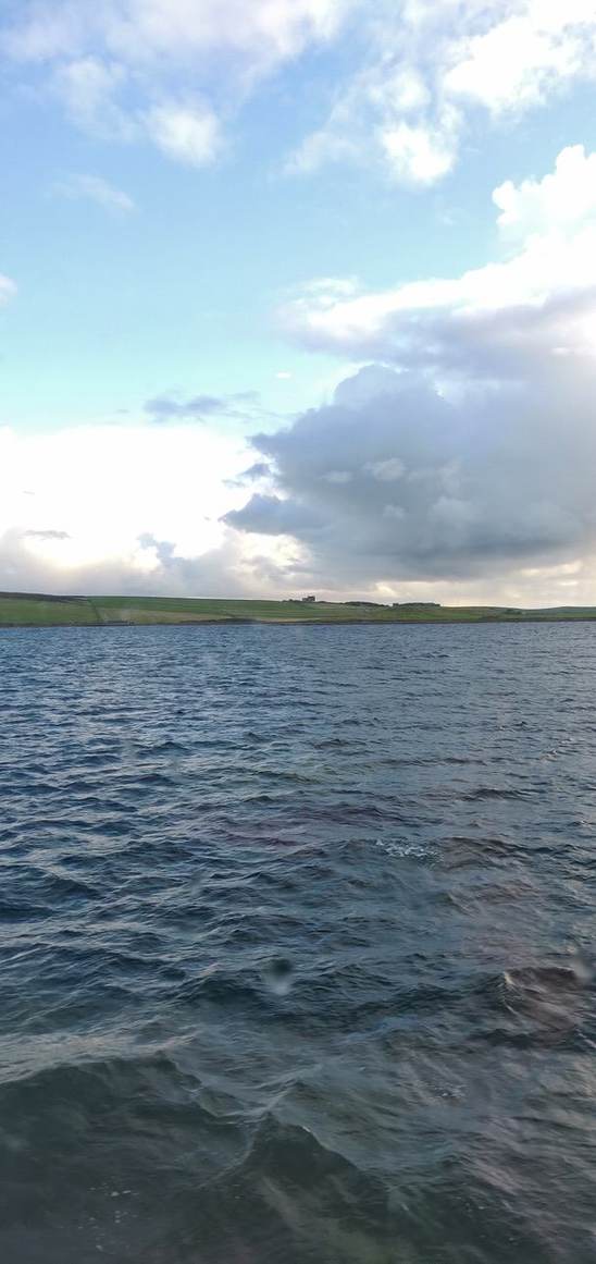 Blue sea beneath a green island coastline and a sky filled with sunlit clouds