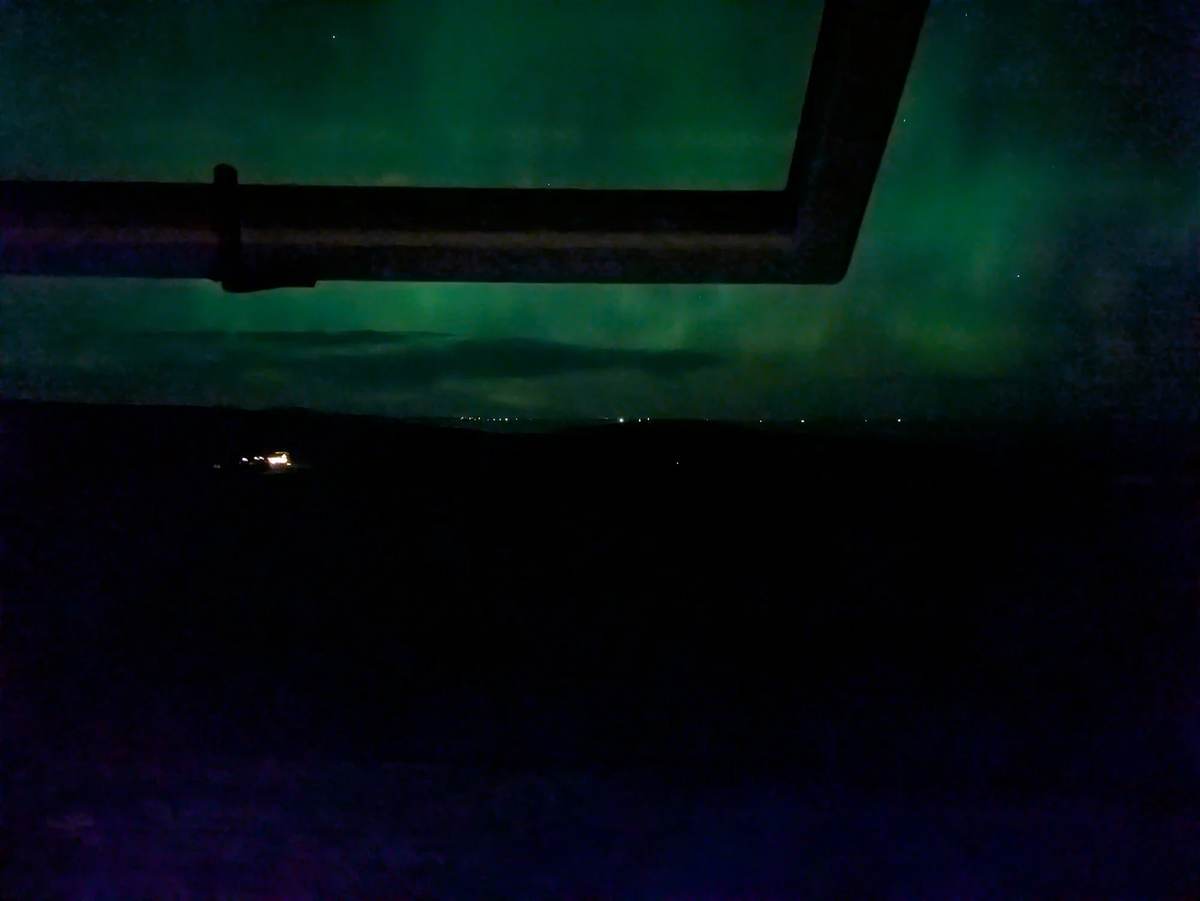 Green northern lights above a dark landscape, framed by an open cottage window