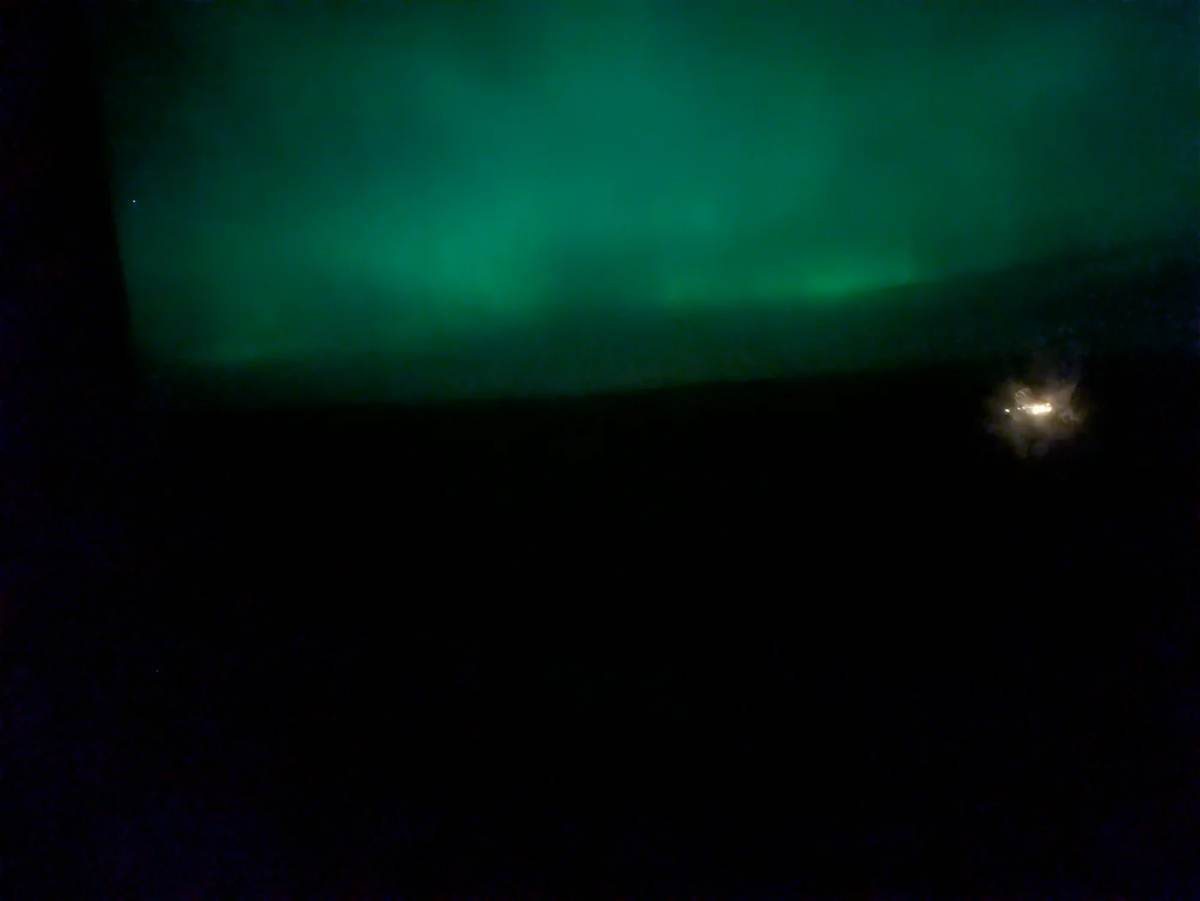 Green northern lights above the dark landscape, seen from the cottages on Rousay