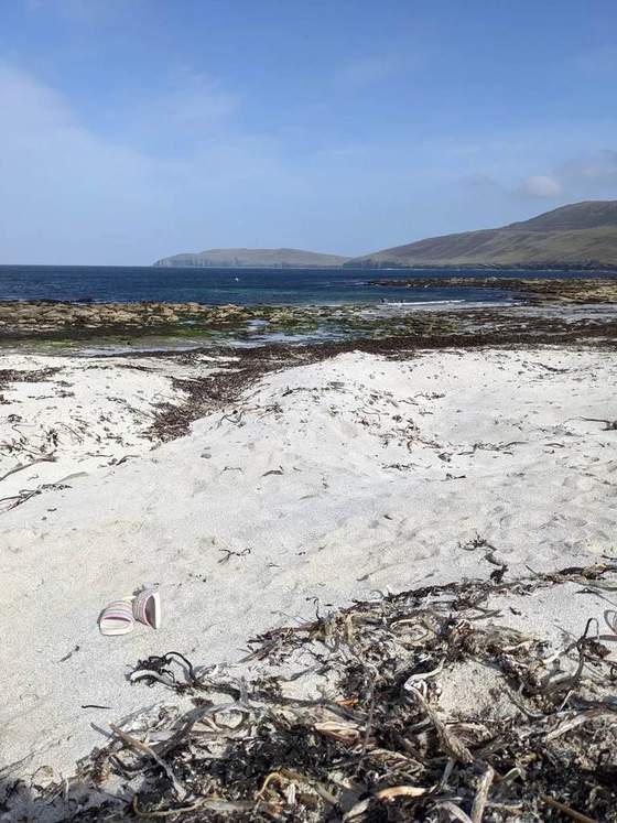 Pale sand and a rocky shoreline, with blue sea and hills beyond