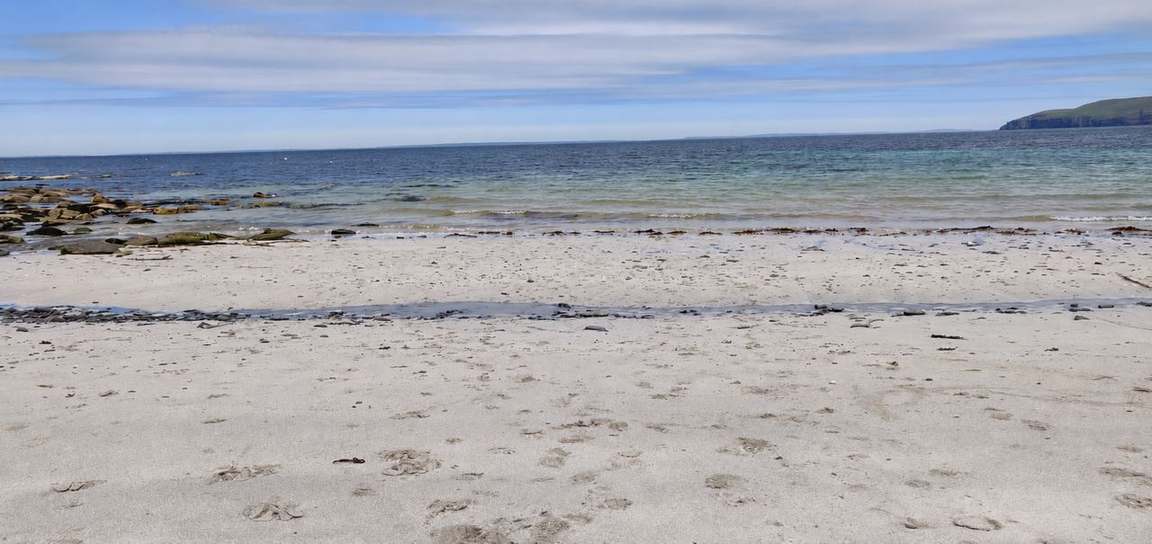 Pale sand and gentle waves at Saviskaill beach, with rocks to the left and a headland beyond