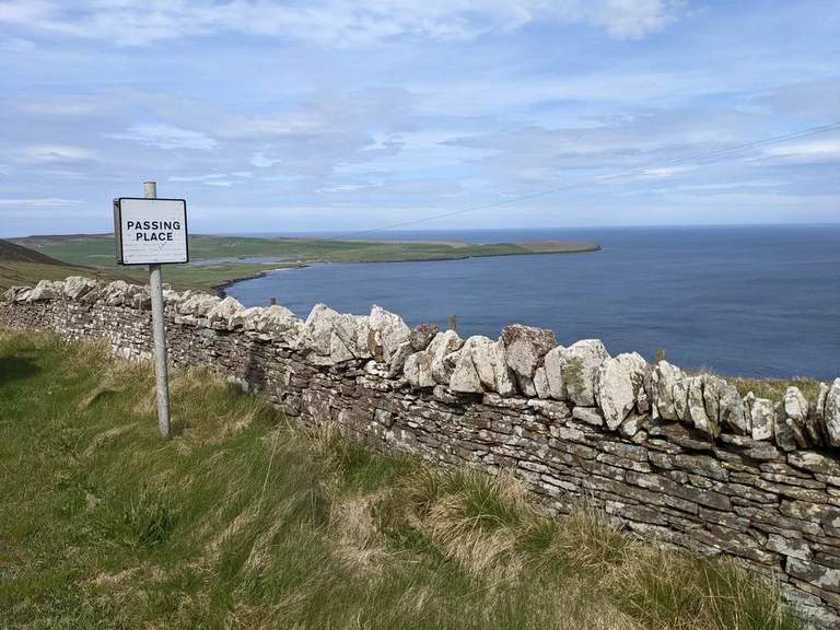 A stone wall and passing-place sign overlooking Saviskaill Bay and the distant coastline on Rousay