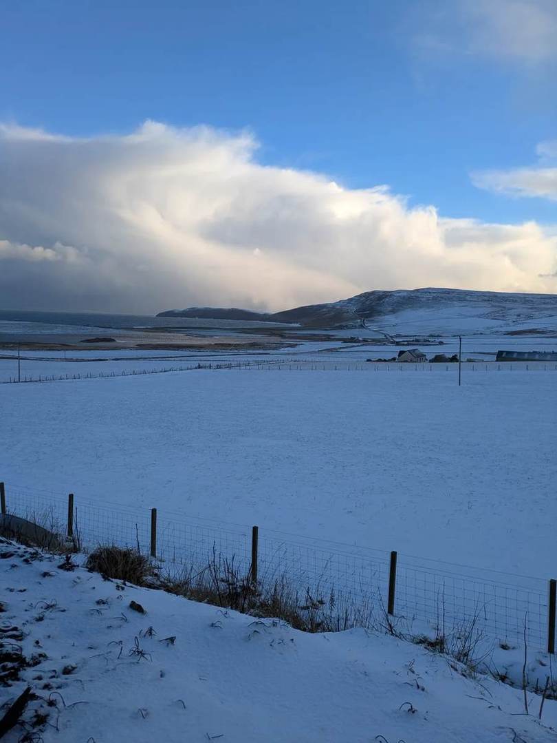 Snowy fields above a loch and the sea on Rousay, with a hillside beneath sweeping white cloud