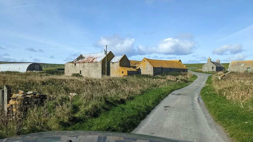 Stone buildings with weathered roofs beside a narrow winding road on Rousay