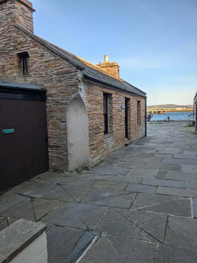 Flagstone lane beside a stone building, leading to Stromness harbour